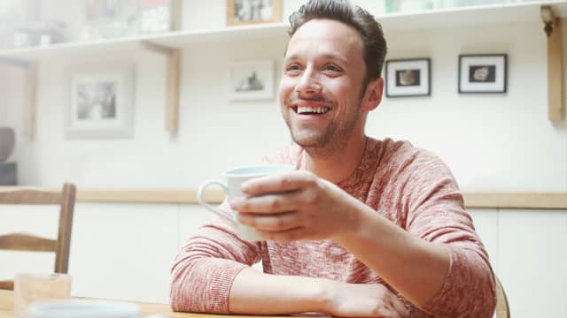  בחור מחייך ומחזיק כוס קפה להמחשת סיבות להיווצרות אבן בשיניים