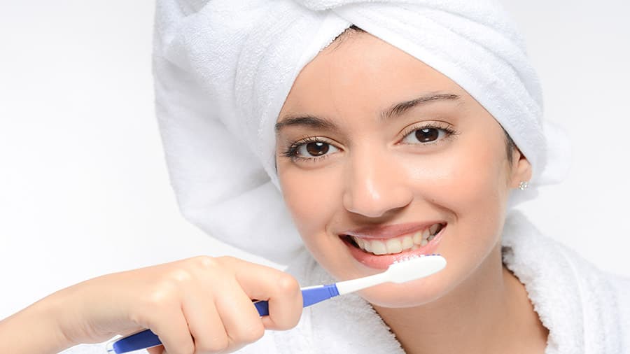 אישה עם מברשת שיניים מברשת את שינייםיה בחדר אמבטיה.