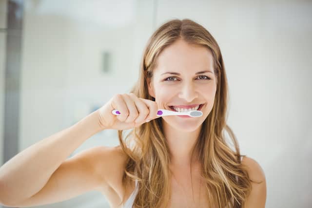 אישה מצחצחת שיניים כי היא מבינה איך למנוע ריח רע מפה