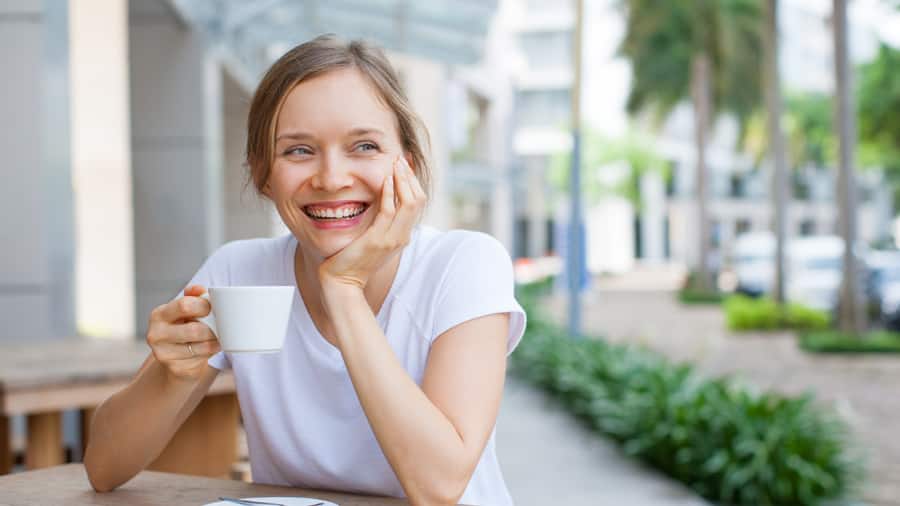 אישה שותה קפה ומחייכת כי היא למדה איך למנוע כתמי קפה בשיניים