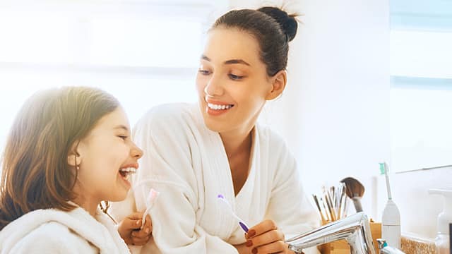 אמא המלמדת את בתה הצעירה כיצד להשתמש בחוט דנטלי בשיניים