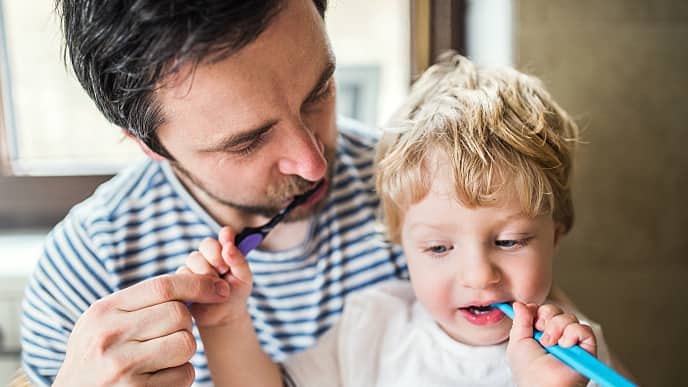 אב ובן מצחצחים שיניים להמחשה של ניקוי אבן בשיניים